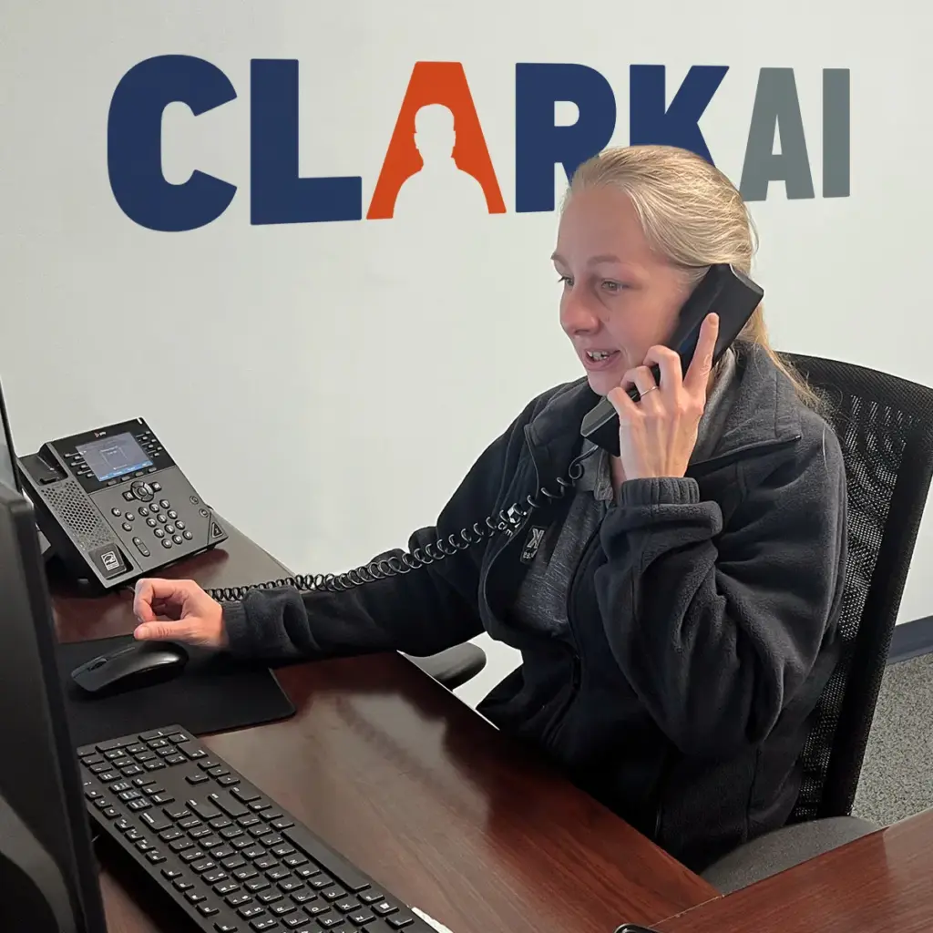 CLARK AI Managed Services image of Shawn taking calls with CLARK AI logo on the wall in the background.